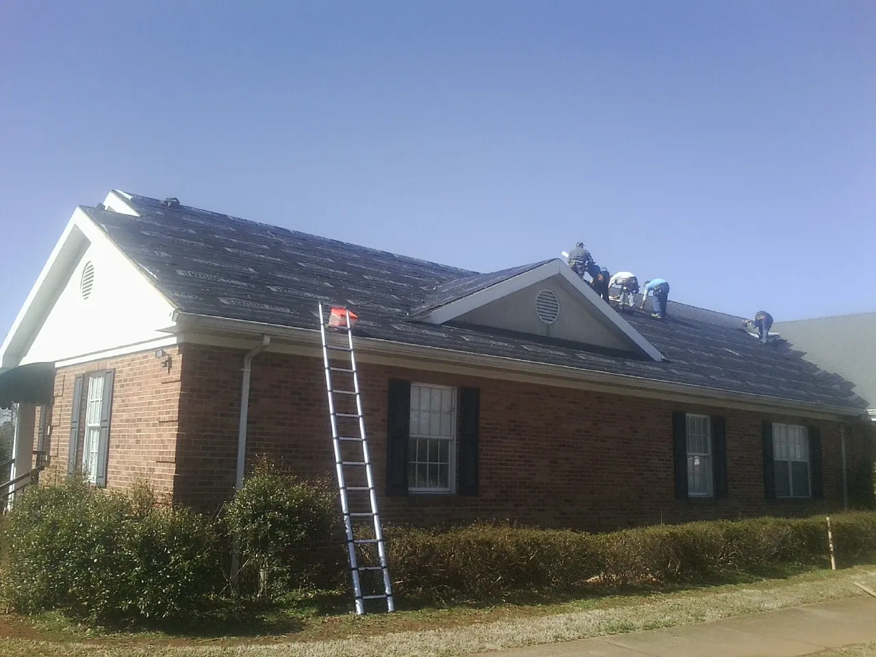 Crew tearing shingles off a brick ranch roof with a ladder set — Metal Roof Repair work by our crew in Columbus City
