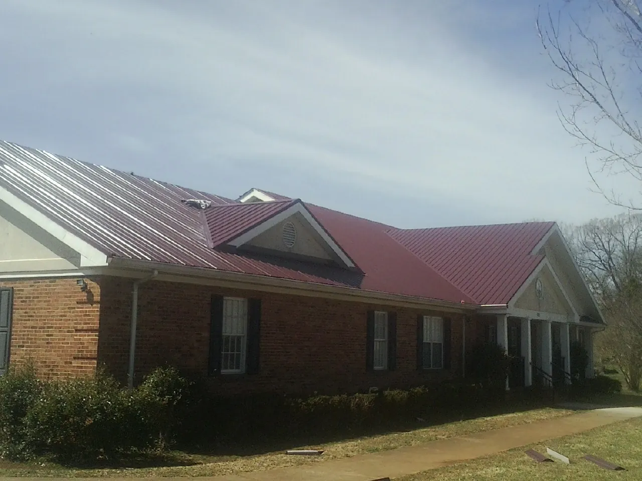 Red metal roof with gabled entries on a long brick building, from a Hail Damage Roof Repair job in Columbus City
