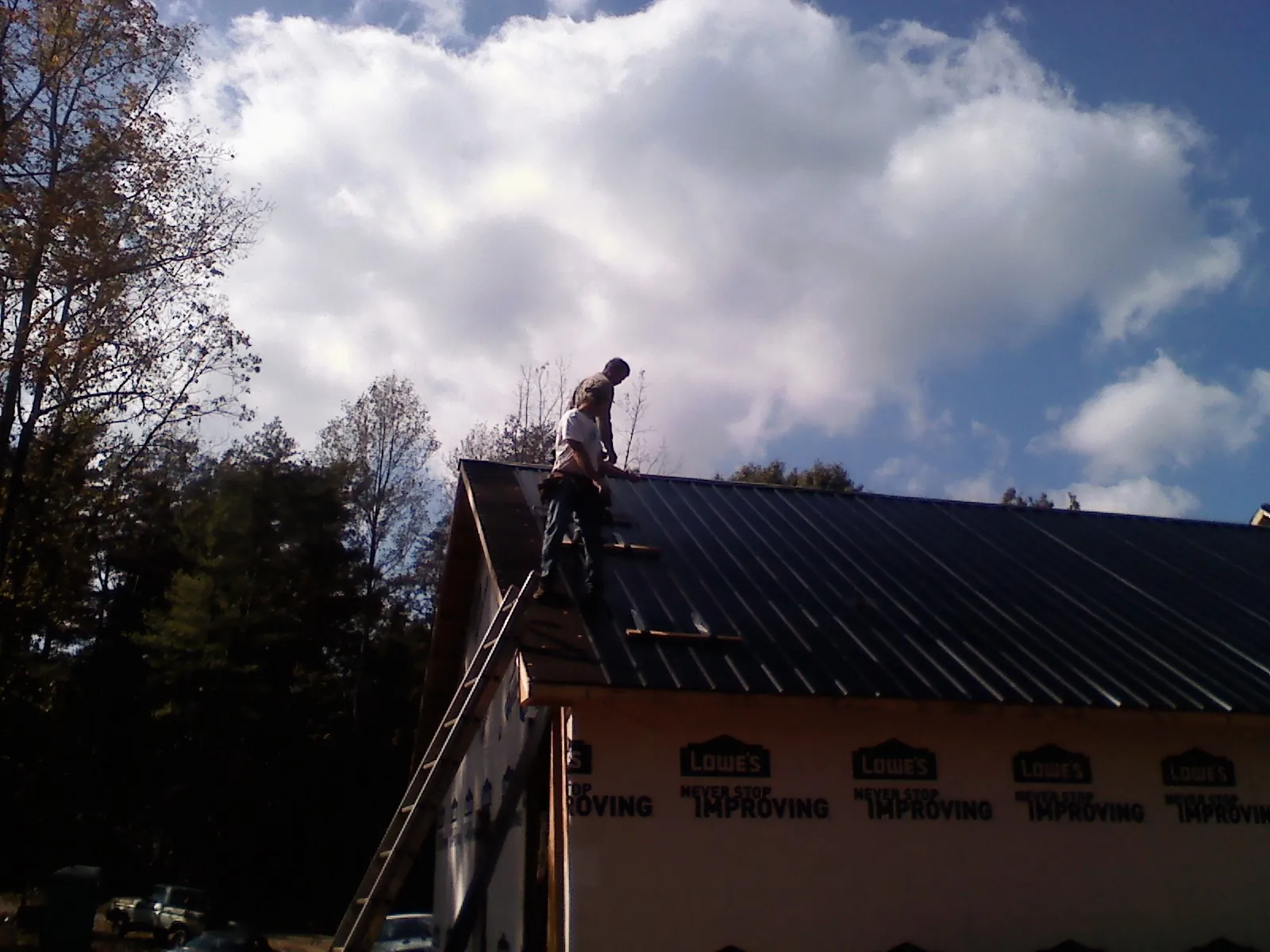 Roofer fastening dark metal panels high against a cloudy sky, from a Roof Inspection job in Columbus City