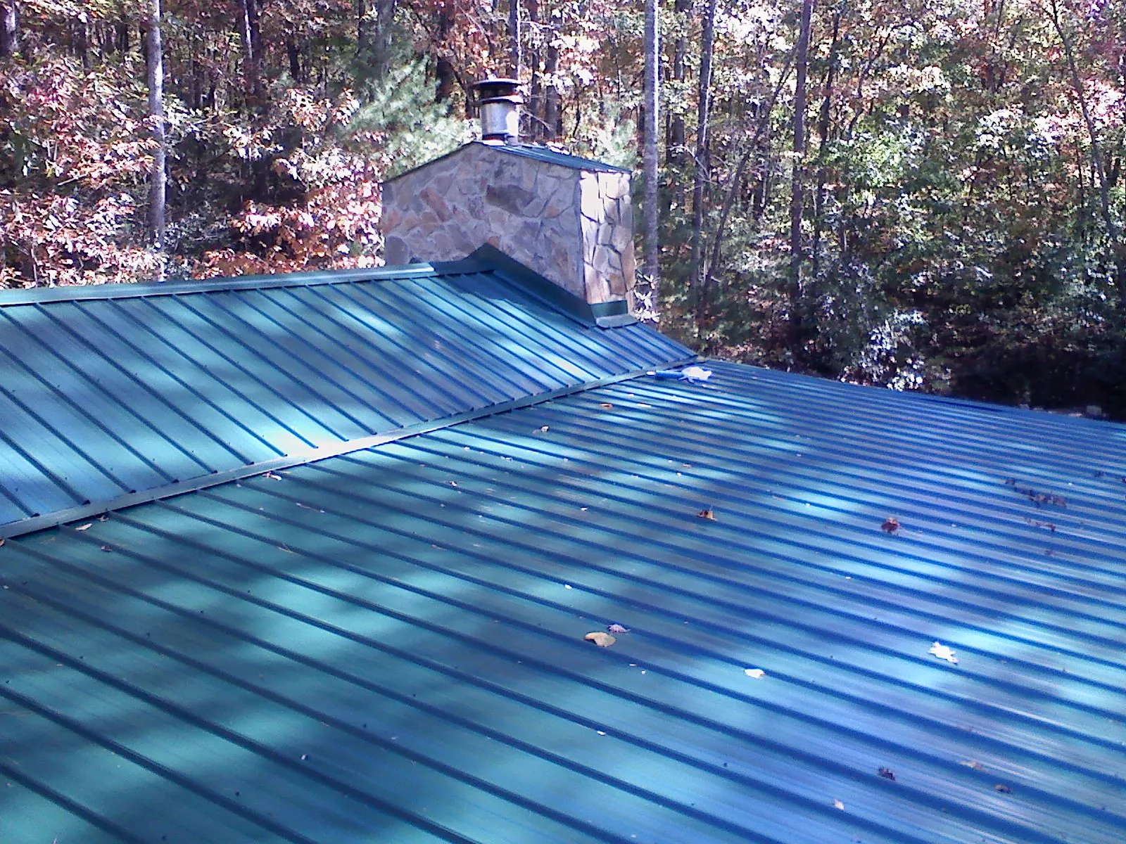 New green metal roof and stone chimney surrounded by autumn woods in Columbus City