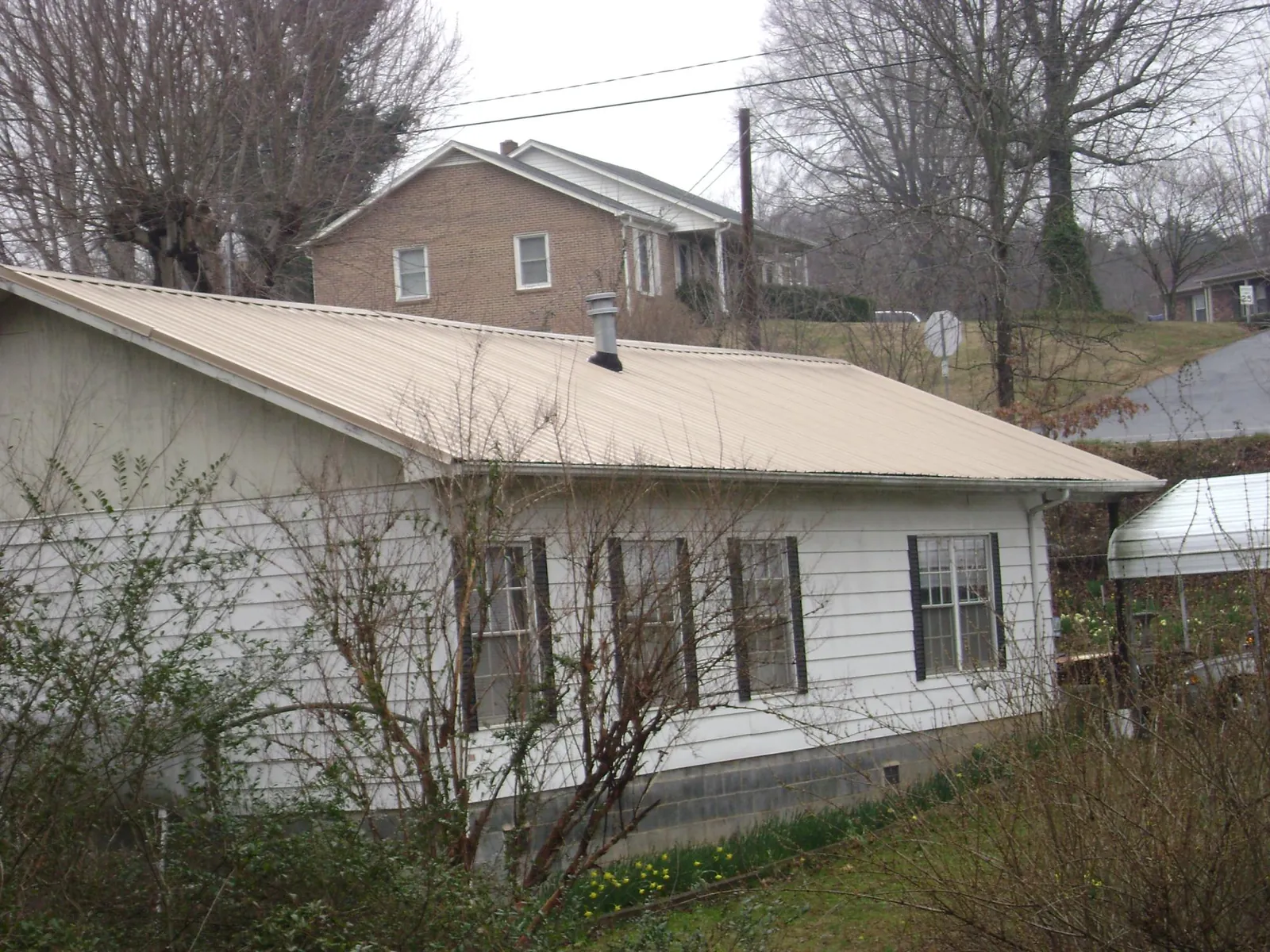 Tan metal roof on a white sided house set into a hillside — Commercial Roofing by Roofing Brothers in Columbus City